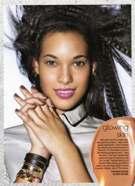 Close-up of a woman with crimped dark hair wearing a neutral blouse with black trim, bracelets, and lipstick; beauty editorial.
