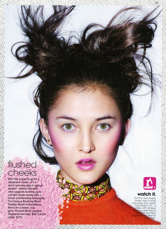 Close-up portrait of a young woman with updo hairstyle, wearing makeup and a patterned top, against a halftone background.