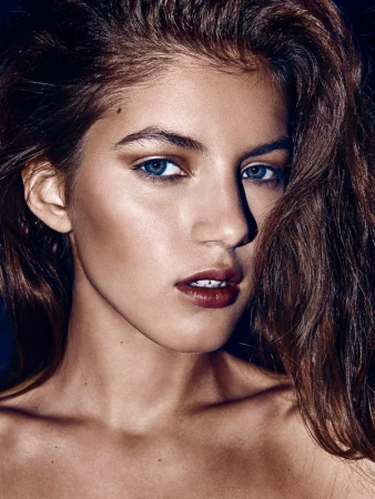 Close-up portrait of a woman with long brown hair, blue eyes, and dark lipstick, styled by Jenna Menard.