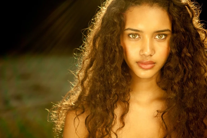 Close up portrait of a woman with long dark curly hair and warm lighting by make up artist Jenna Menard
