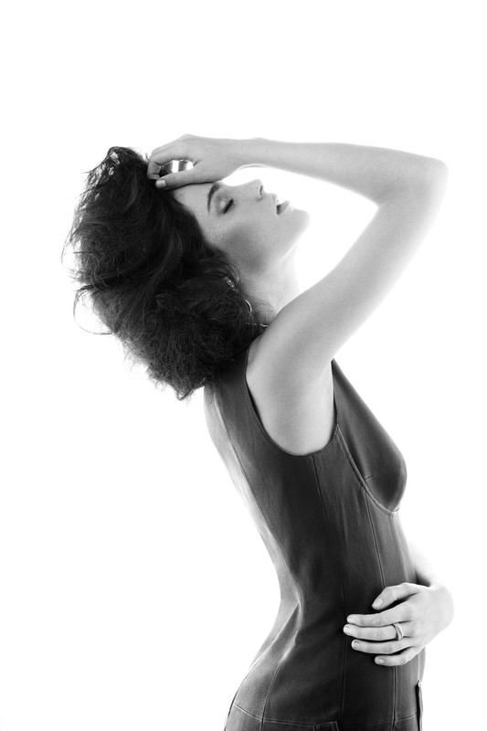 Monochrome portrait of an adult woman in sleeveless top, eyes closed and head tilted back against a bright white background.