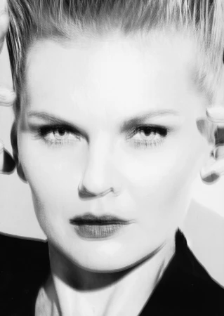 Close-up black and white portrait of a blonde woman with dark lipstick pulling back her hair, styled by Jenna Menard.