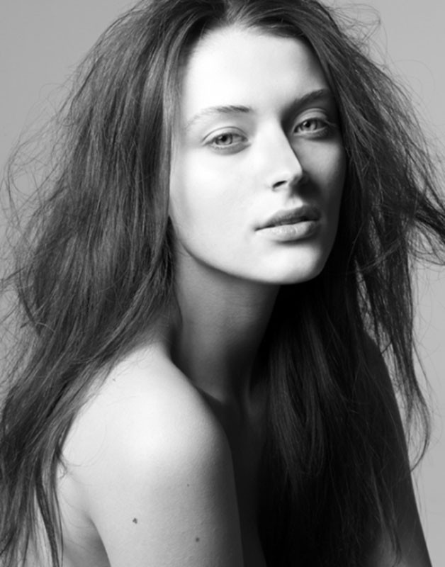 Monochrome beauty portrait of a woman with long tousled hair and natural makeup against a plain background