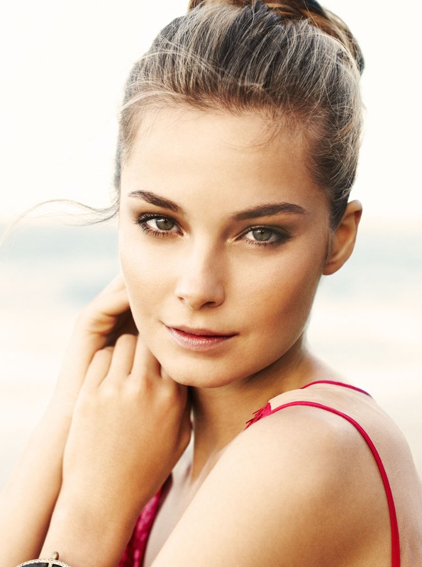 Close-up portrait of a woman with her hair in a bun, wearing a pink top with thin straps, with makeup by Jenna Menard
