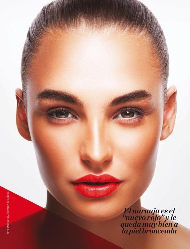 Close-up portrait of a woman with glowing skin, wearing red lipstick, against a bright background. Beauty and makeup concept.