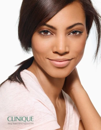 Close-up of an adult female model with dark hair and a light pink shirt in a beauty advertisement with skincare branding.