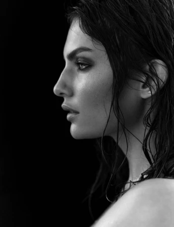 Black and white profile portrait of a woman with wet hair and dramatic makeup against a dark background
