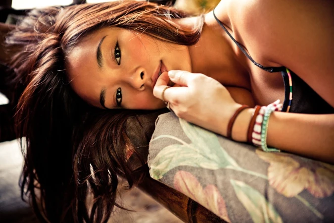 Close-up portrait of a young woman lying down with dark hair, wearing stacked bracelets and a dark strap top.