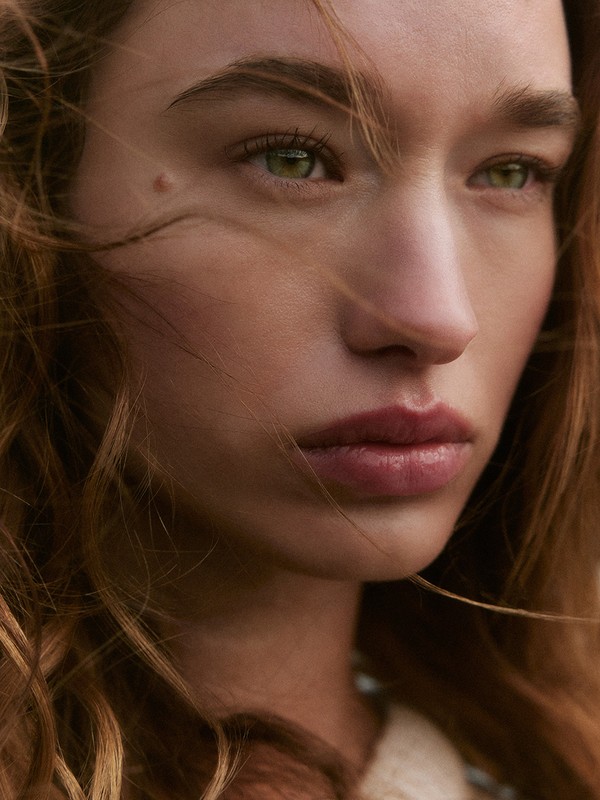 Close-up portrait of a fair-skinned woman with wavy blonde hair, green eyes, and soft lighting in an outdoor setting.