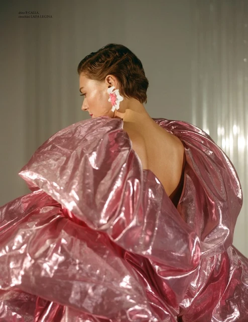 Back view of a stylish adult woman with short brown hair, wearing a metallic pink, voluminous dress, and white flower earrings.