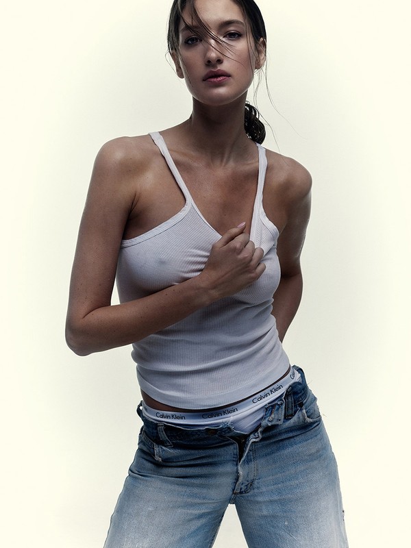 Woman in a tank top and jeans poses in a studio environment. She has wet hair. Visible Calvin Klein underwear waist band.