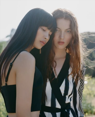 Two female models posing closely together outdoors in soft daylight with hair styling by Jennifer Budner