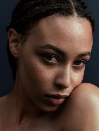 Close-up portrait of a woman with braided hair and natural skin texture against a dark background