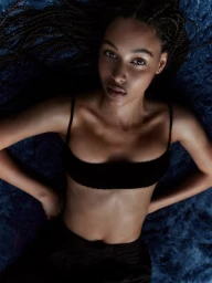 Overhead portrait of a young woman with braided hair lying on a textured blue rug wearing a dark top.
