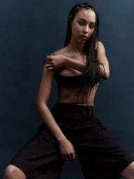 Portrait of a black woman with long braided hair wearing dark shorts and top against a blue studio background