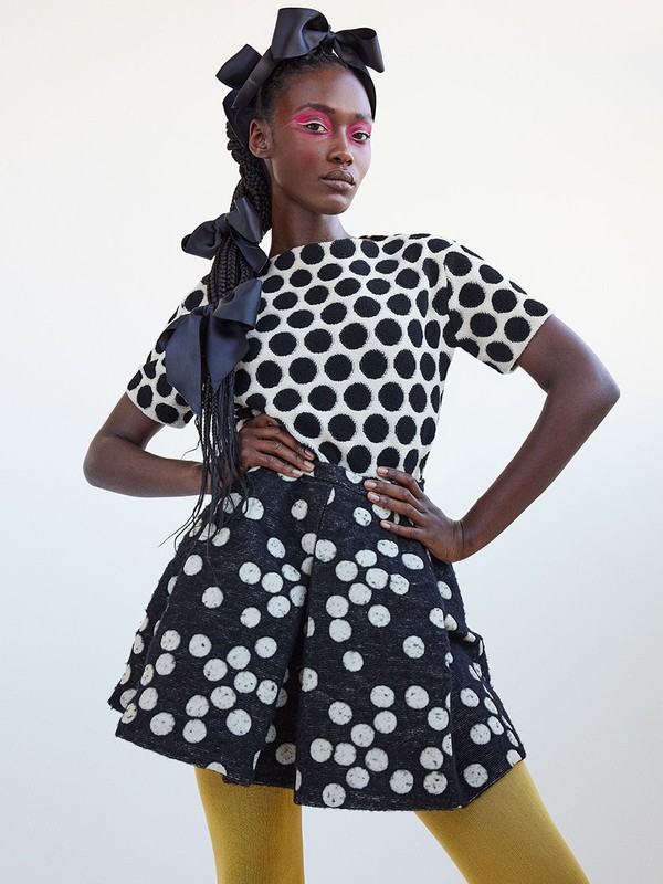 Woman in a black and white polka dot outfit poses in a studio. She is wearing large black bows in her hair and on her top.