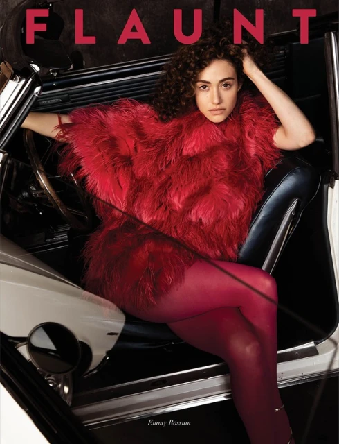 Emmy Rossum poses inside of a car wearing a red faux fur coat and red tights for a magazine cover shoot.