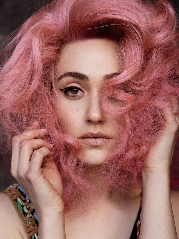 Close-up portrait of a woman with voluminous textured pink hair and winged eyeliner framing her face.