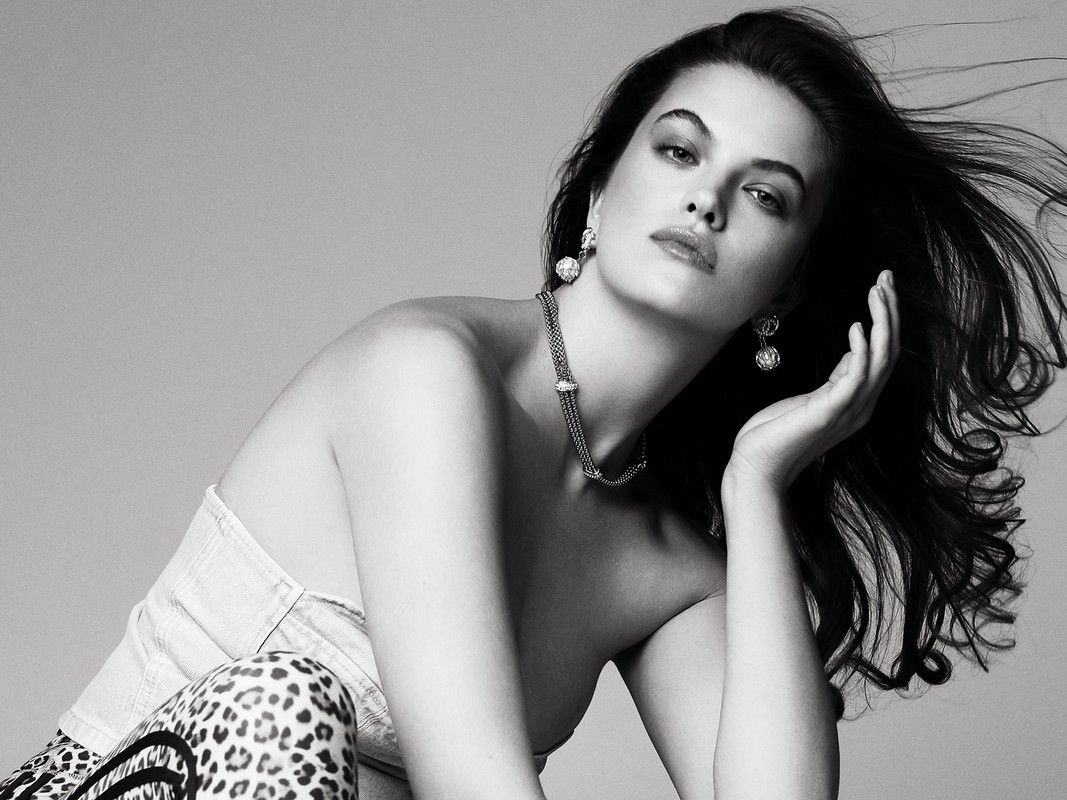 Black and white portrait of a woman wearing jewelry, posing in a strapless top with leopard print bottoms against a gray backdrop.