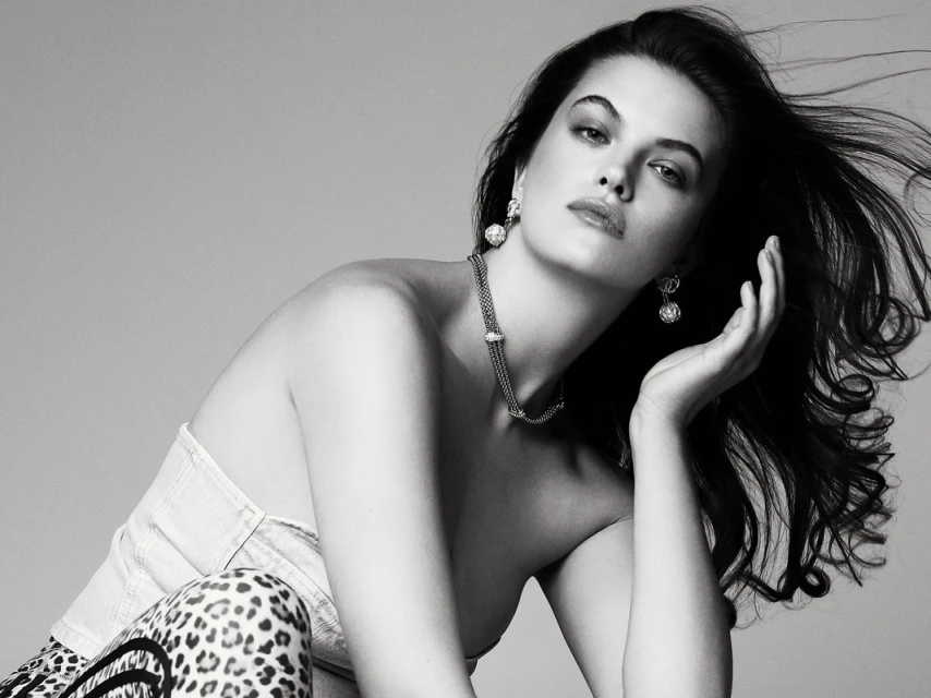 Black and white portrait of a woman wearing jewelry, posing in a strapless top with leopard print bottoms against a gray backdrop.