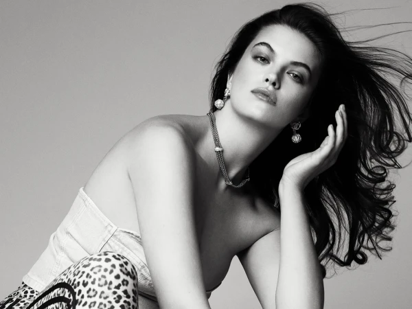 Black and white portrait of a woman wearing jewelry, posing in a strapless top with leopard print bottoms against a gray backdrop.