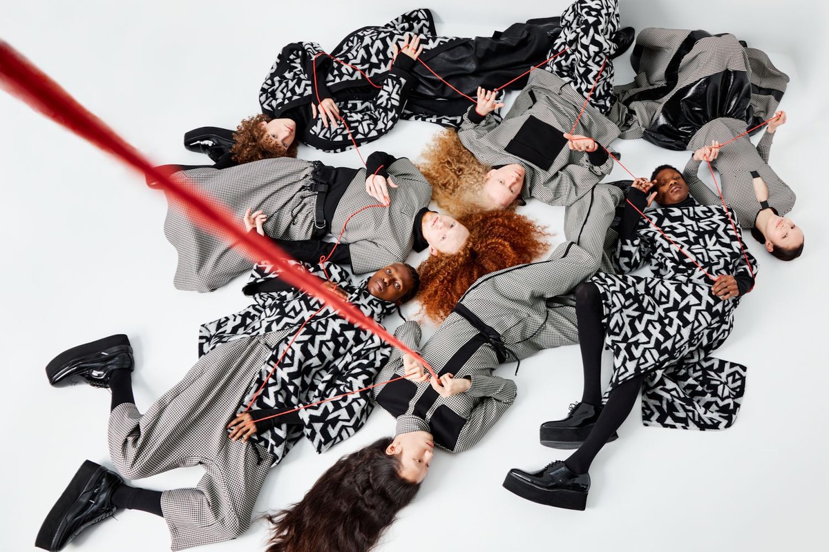 Overhead shot of diverse fashion models lying in a circle on white background, wearing patterned black and white clothing, connected by a red string.