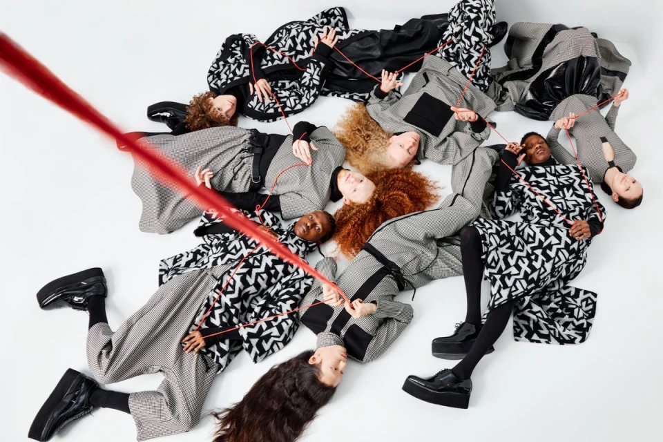 Overhead shot of diverse fashion models lying in a circle on white background, wearing patterned black and white clothing, connected by a red string.
