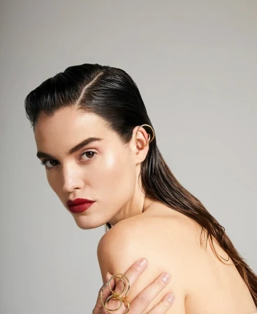 Close-up of a woman with wet hair, red lipstick, and gold jewelry, posing in a studio setting with a neutral background, beauty shot.