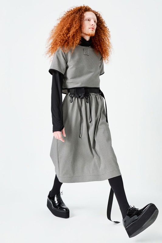 Model with red curly hair wearing houndstooth outfit and platform shoes against white background