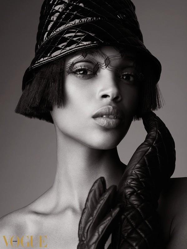 Close-up black and white studio shot of a Black female fashion model wearing a quilted hat, black gloves, and editorial makeup.