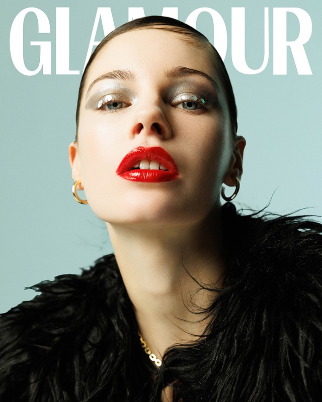 Glamour magazine cover featuring a woman with glitter eyeshadow and red lipstick, wearing a black furry garment, against a blue backdrop.