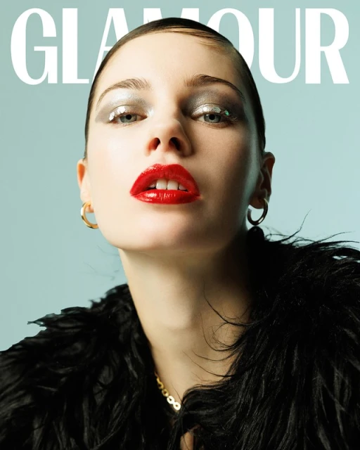 Glamour magazine cover featuring a woman with glitter eyeshadow and red lipstick, wearing a black furry garment, against a blue backdrop.