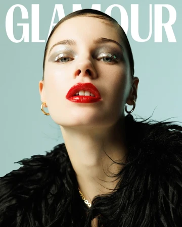Glamour magazine cover featuring a woman with glitter eyeshadow and red lipstick, wearing a black furry garment, against a blue backdrop.