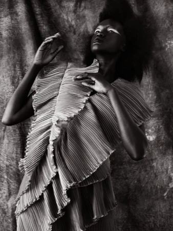 Black and white editorial portrait of a woman in a pleated textured top against a textured background by Jennifer Covington-bowers