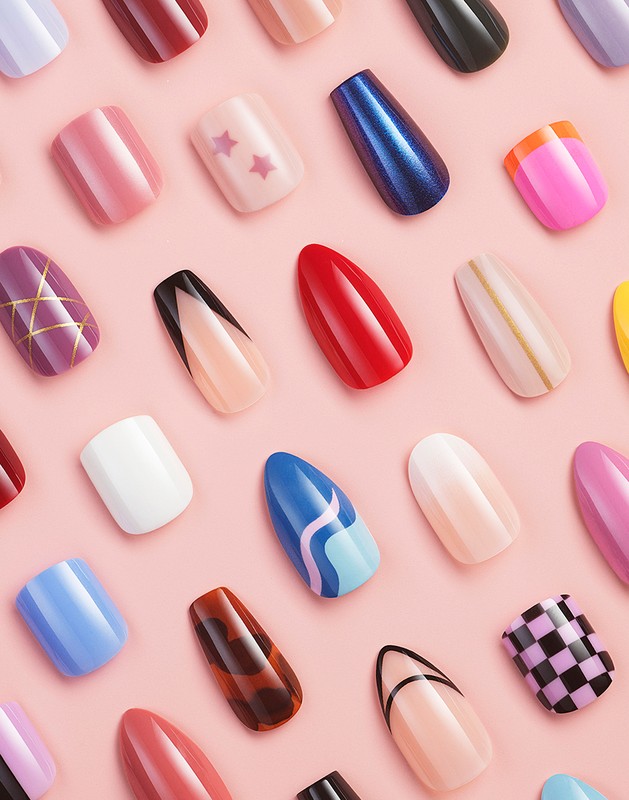 Overhead shot of an assortment of varied, colorful, artificial fingernails arranged in rows against a plain pink background.