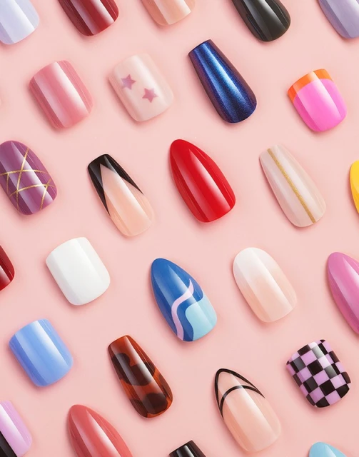 Overhead shot of an assortment of varied, colorful, artificial fingernails arranged in rows against a plain pink background.