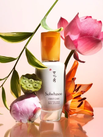 Sulwhasoo First Care Activating Serum product shot with white bottle, amber cap, pink peonies, tiger lily, water lily, and green foliage.