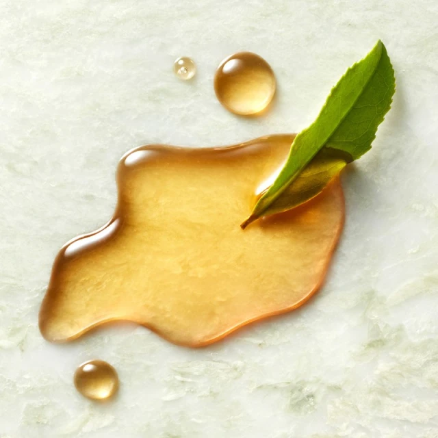 Close-up of liquid and green leaf on a light green marble surface, showcasing textures, light reflection, and natural elements.