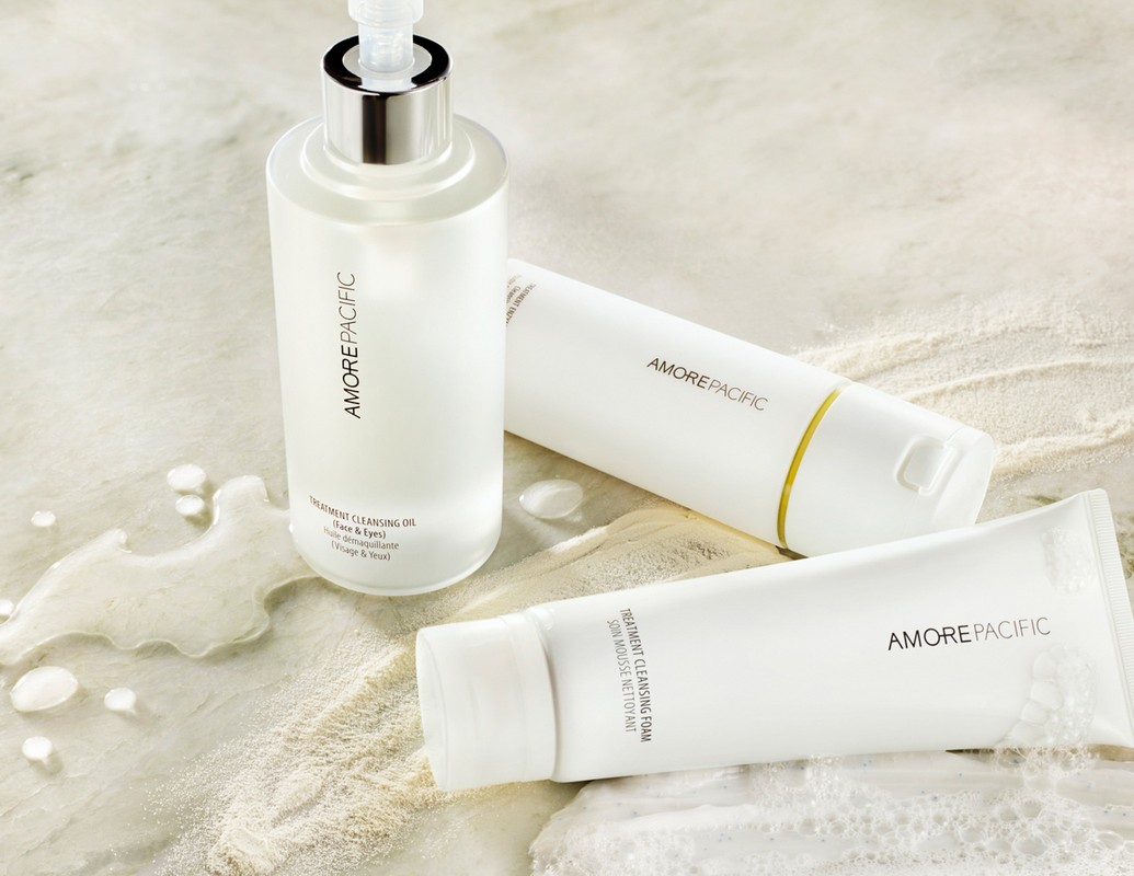 Product shot featuring AmorePacific cleansing oil and foam products in white packaging on a light marble surface with water droplets.