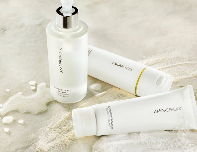 Product shot featuring AmorePacific cleansing oil and foam products in white packaging on a light marble surface with water droplets.