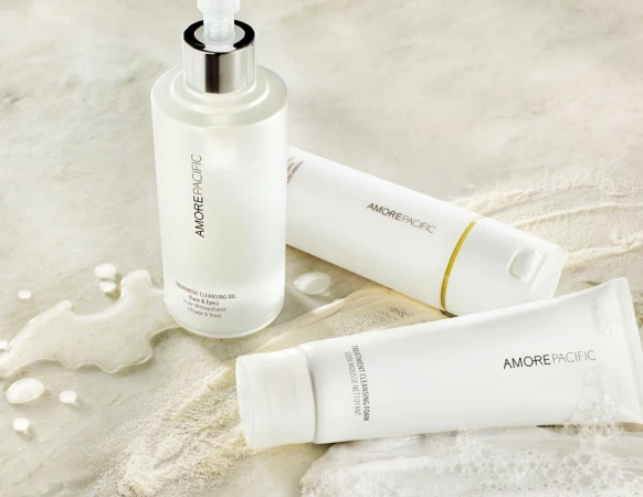 Product shot featuring AmorePacific cleansing oil and foam products in white packaging on a light marble surface with water droplets.