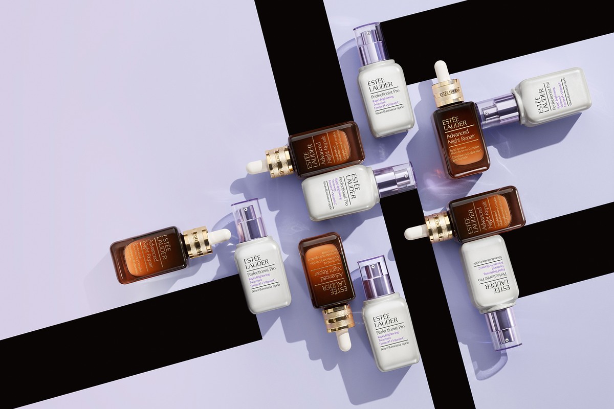 Overhead product shot of Estee Lauder skincare products including Advanced Night Repair and Perfectionist Pro serums, against a light purple backdrop.