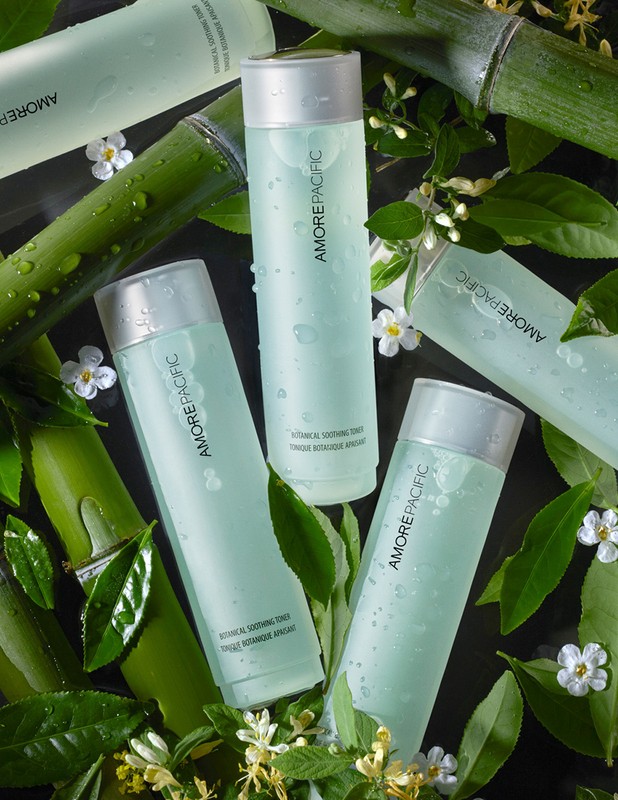 Botanical skincare product bottles from Amorepacific arranged with fresh green bamboo stalks and white flowers for a beauty advertisement.