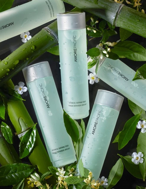 Botanical skincare product bottles from Amorepacific arranged with fresh green bamboo stalks and white flowers for a beauty advertisement.