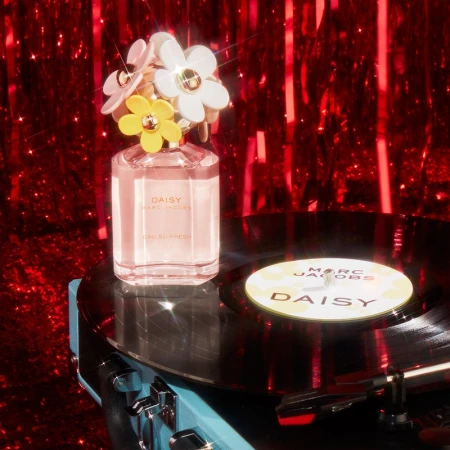 Marc Jacobs Daisy Eau So Fresh perfume bottle on a record player with red glitter background, emphasizing floral design and brand.