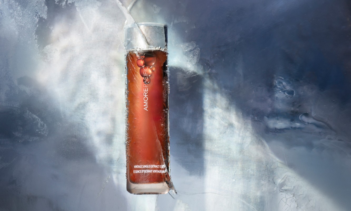 Studio shot of Amorepacific vintage essence in transparent bottle, encased in ice with grey and white background.