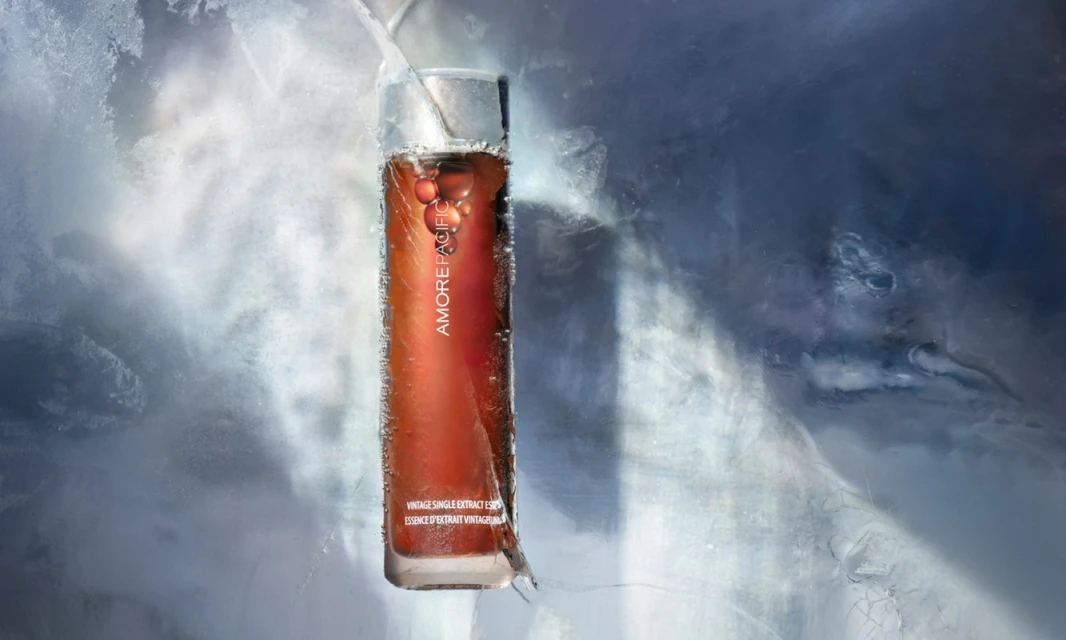 Studio shot of Amorepacific vintage essence in transparent bottle, encased in ice with grey and white background.
