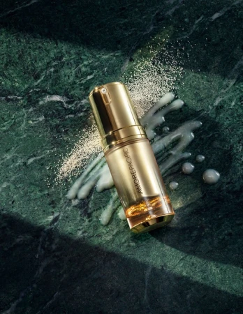 Gold Amorepacific serum bottle on green marble with scattered powder and liquid for beauty and skincare advertising, product photography.