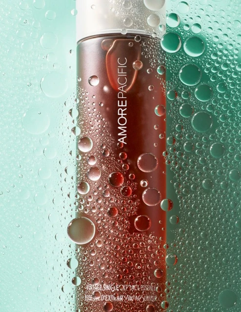Amorepacific skincare product bottle close-up with water droplets against a soft green background, promoting beauty and skincare.
