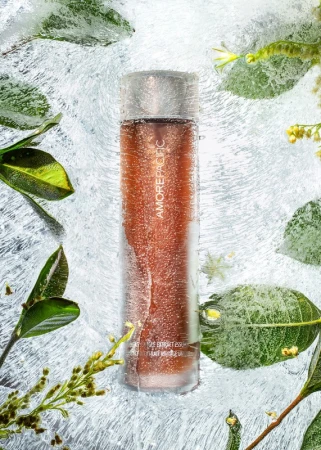 Amorepacific skincare product bottle is surrounded by frosty ice and green leaves, creating a fresh and cool beauty composition.